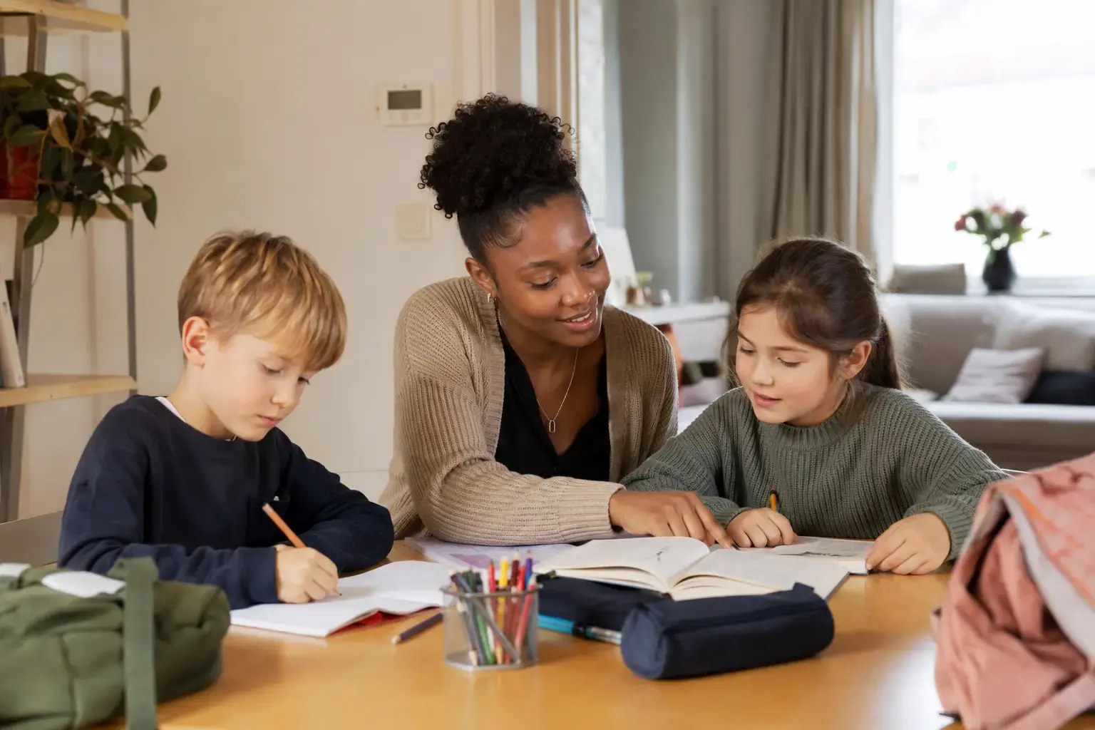 A babysitter helps two children with homework at the kitchen table